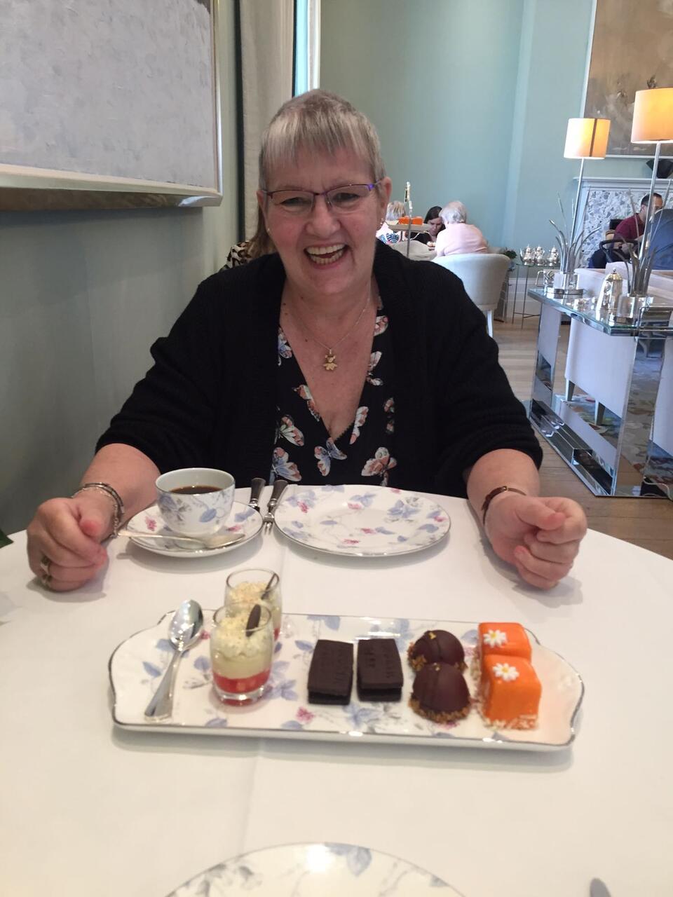 A woman with short grey hair, glasses wearing a dark cardigan at an afternoon tea