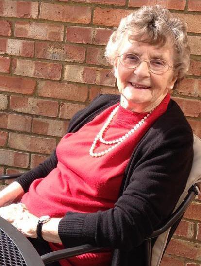A woman with short light hair wearing a red top, black cardigan and glasses