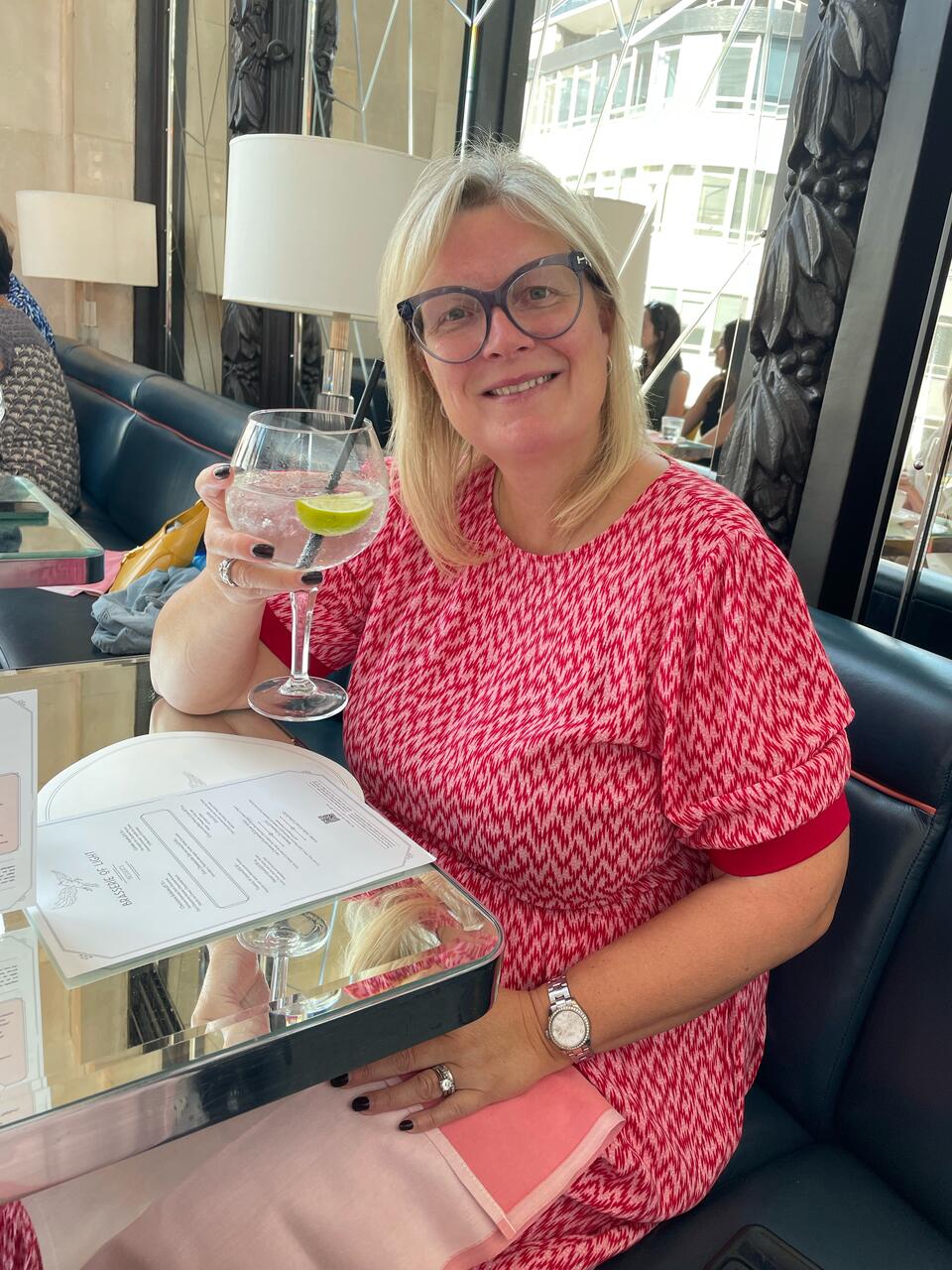 A woman sat at a table, smiling, holding a glass of wine