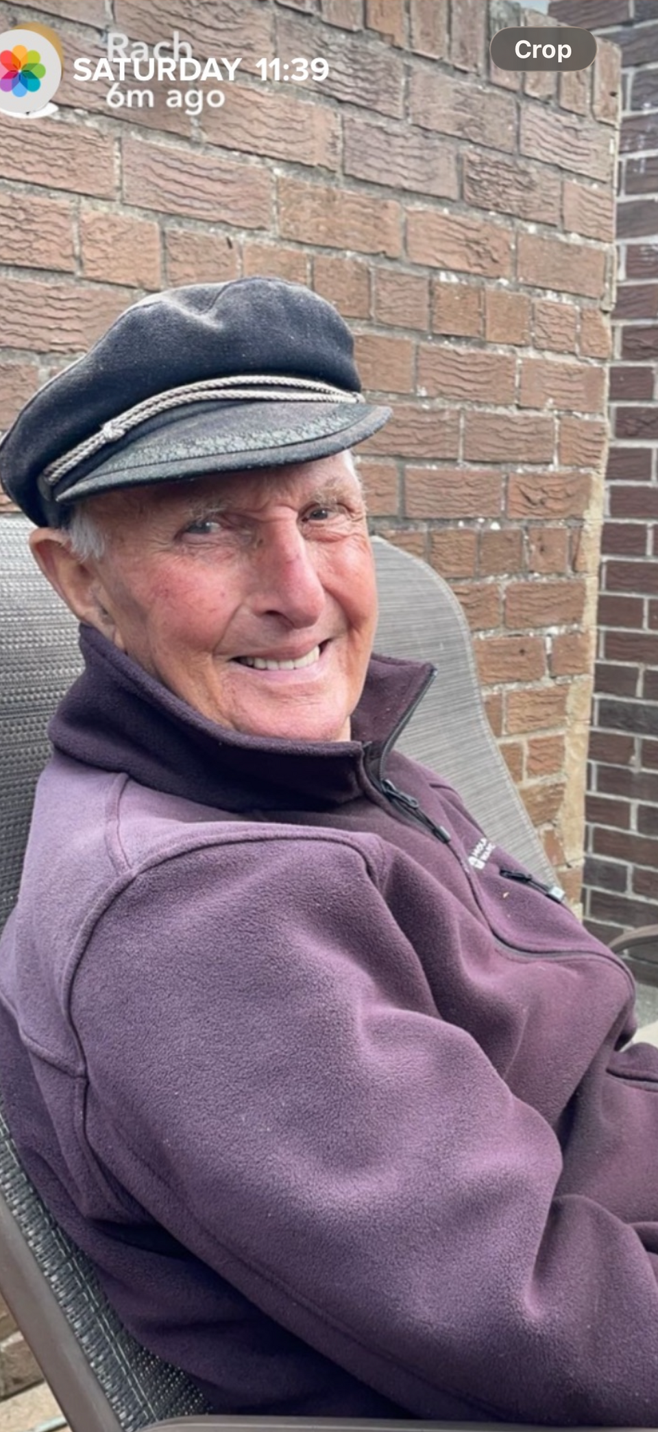A man sat in a chair wearing a green hat and purple fleece