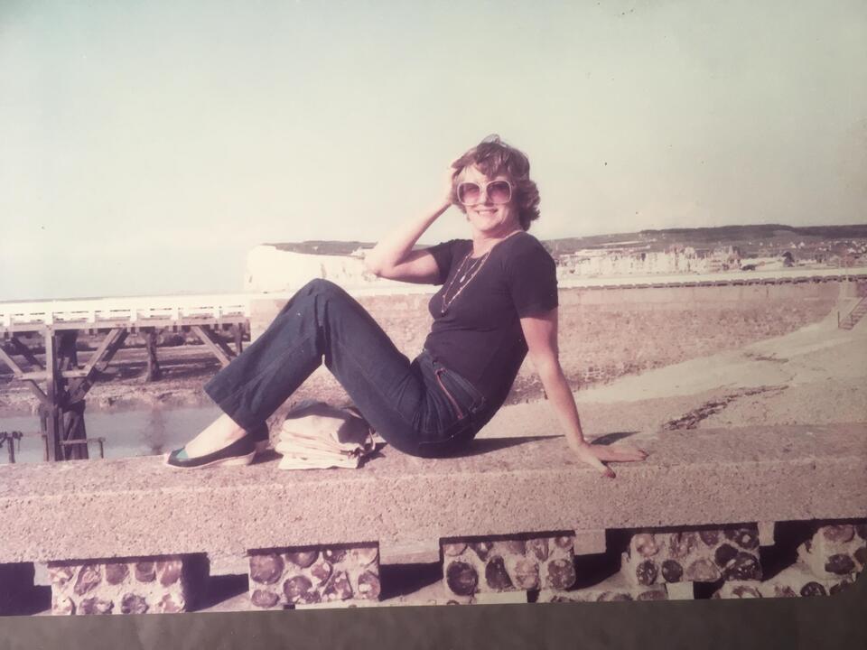 A woman sat on a wall with a beach in the background