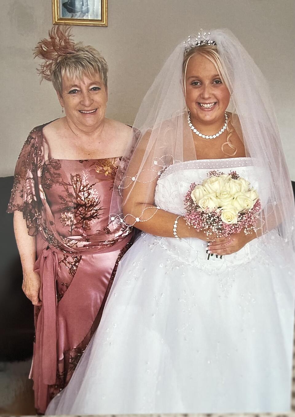 A woman with short blonde hair wearing a pink dress stood next to a bride holding a bouquet