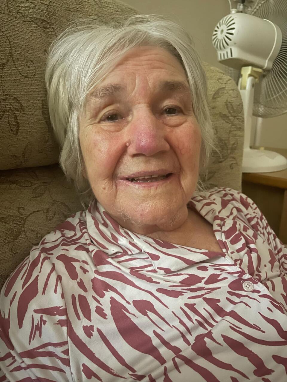 A woman with short white hair wearing a patterned pink and white top