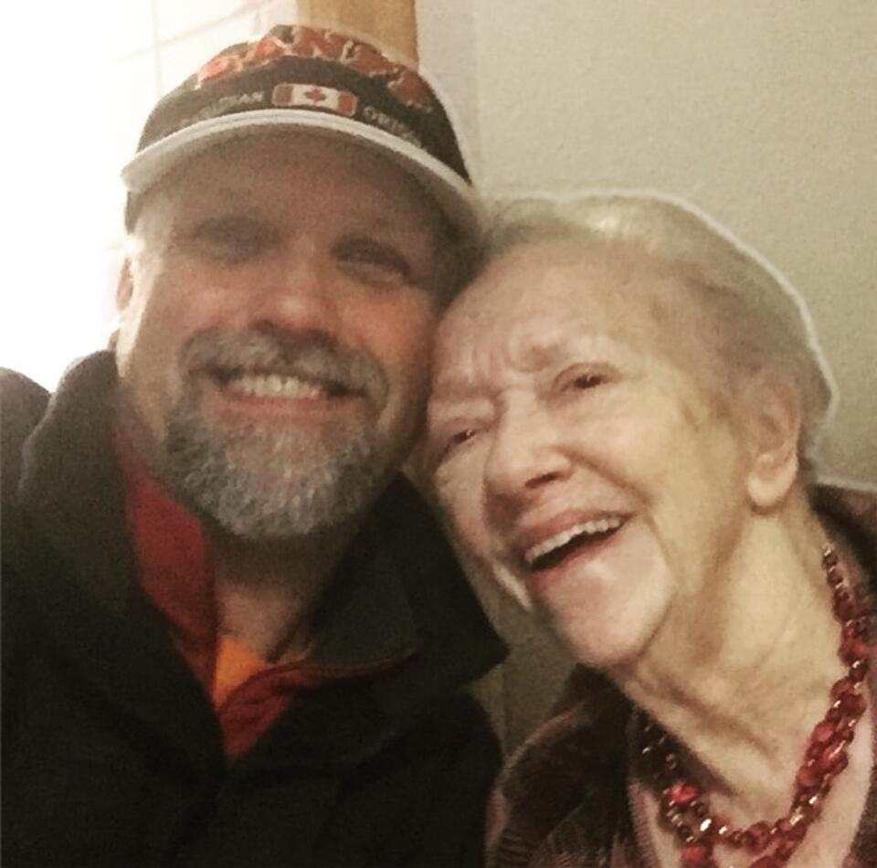 A man wearing a cap and black fleece with a grey beard and a woman with short, light hair wearing a red necklace and dark top