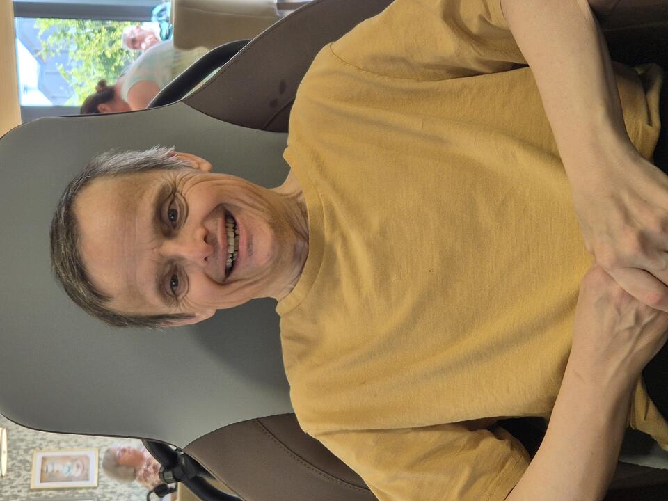 A smiling man wearing a yellow t-shirt sat in a chair