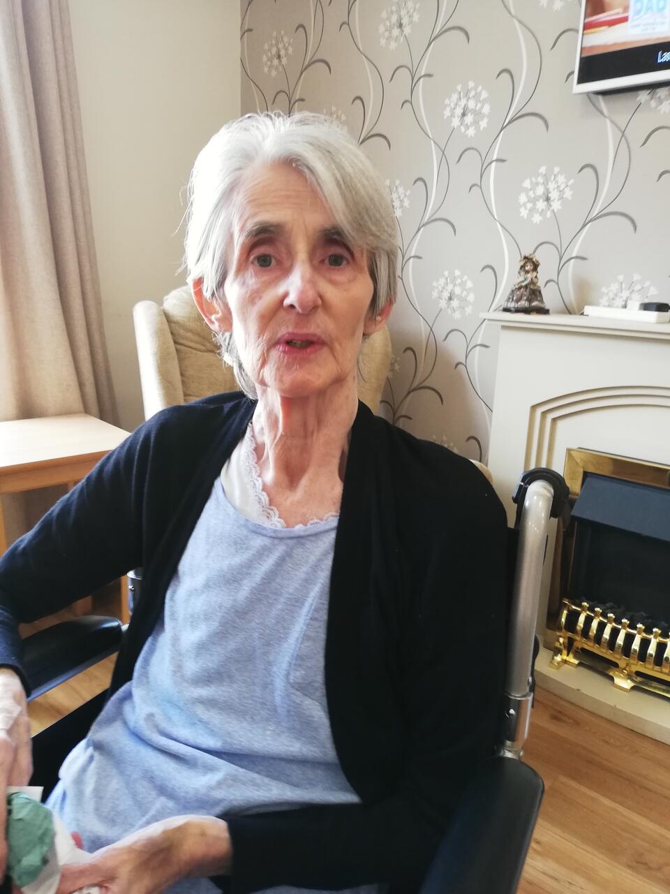 A woman with short grey hair wearing a blue top and black cardigan