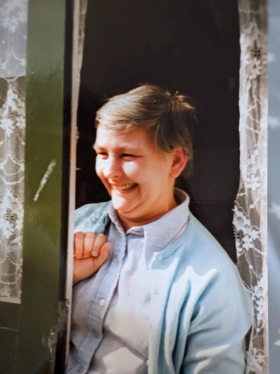 A woman with short dark hair wearing a light shirt and blue cardigan
