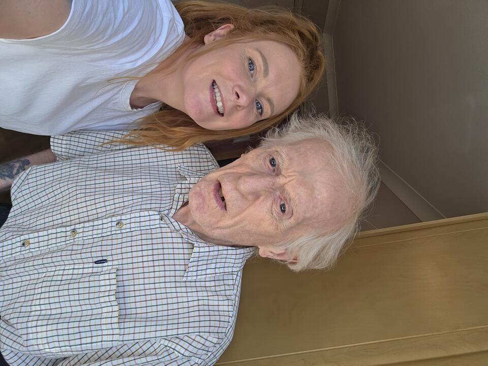 A woman with a ginger ponytail, wearing a white t shirt and a man with white hair wearing a white and green check shirt