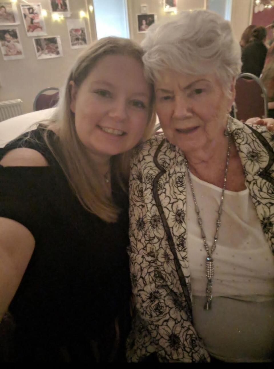 A selfie of a younger woman with blonde hair wearing a black top and an older woman with short white hair, a white top and patterned jacket