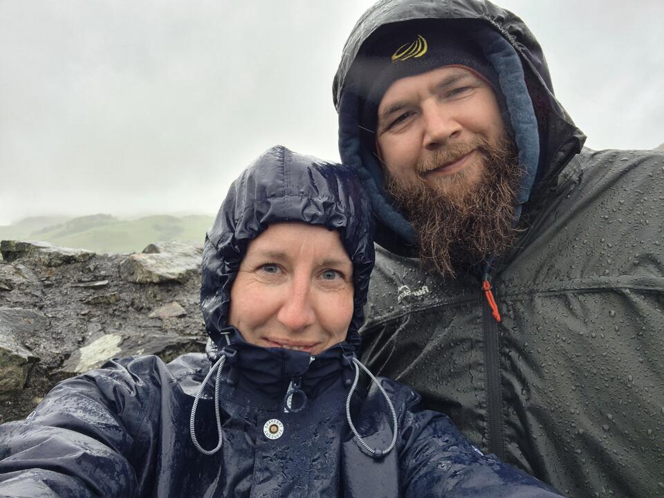 Two people taking a selfie on a mountain wearing wet waterproofs