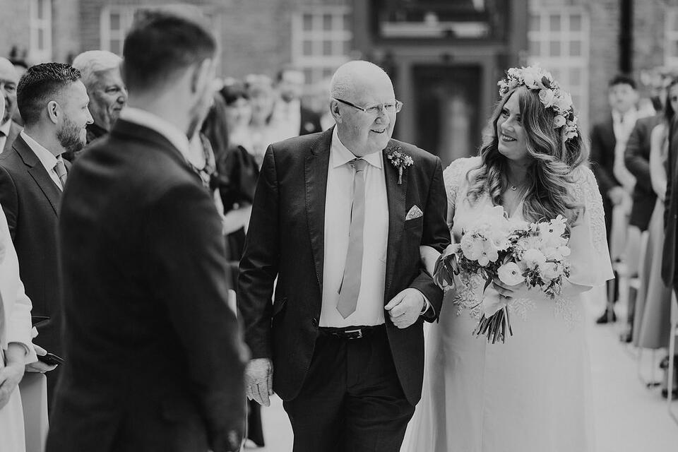 A black and white photo of a man walking a bride down the aisle