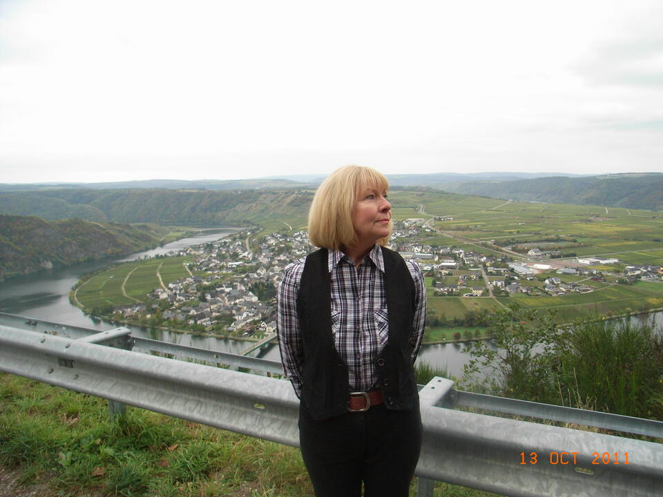 A woman with a short blonde bob and a checked shirt stood on a hill above a town