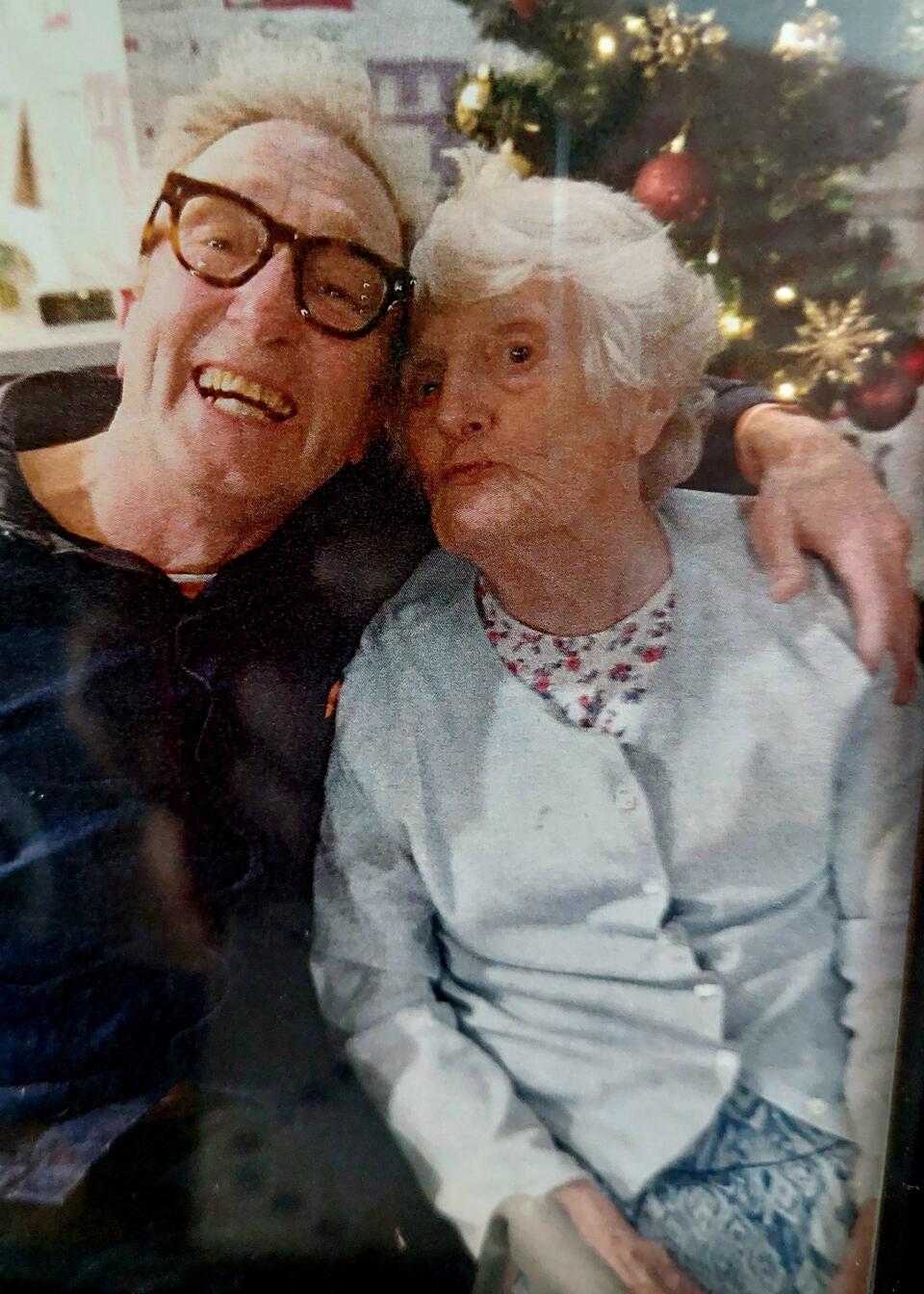 A smiling man hugging an older woman with a Christmas tree in the background
