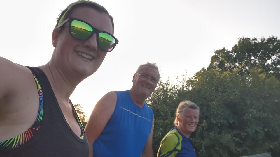 A woman and two men in running clothes with sky and trees behind them