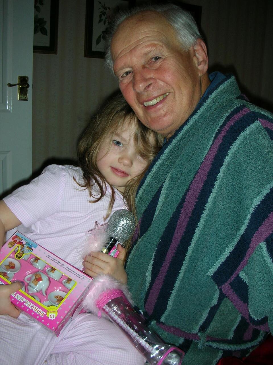 A man with grey hair in a stripy green dressing gown hugging a girl with brown hair and wearing all pink