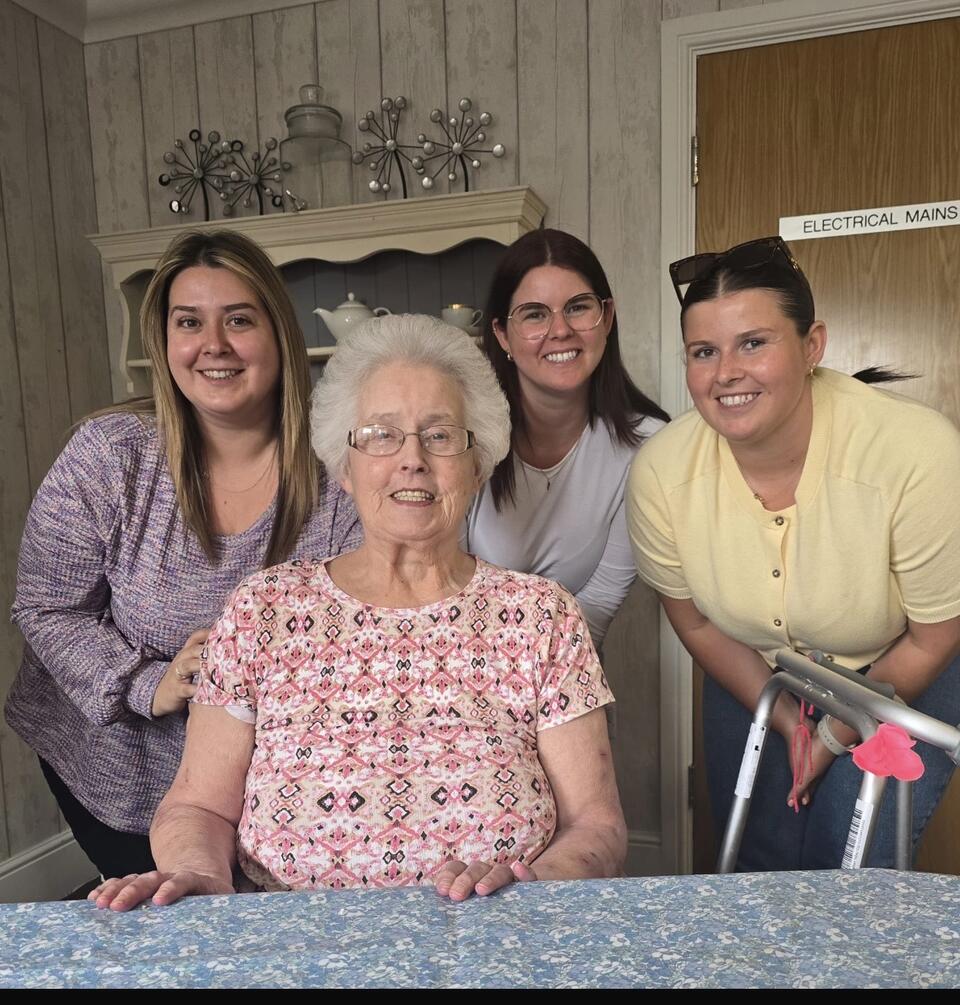 An older woman in the foreground and three younger women stood behind her, all smiling