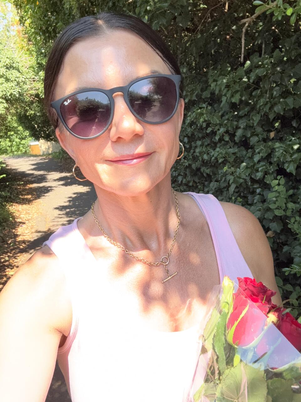 A selfie of a woman wearing sunglasses and holding a bunch of roses