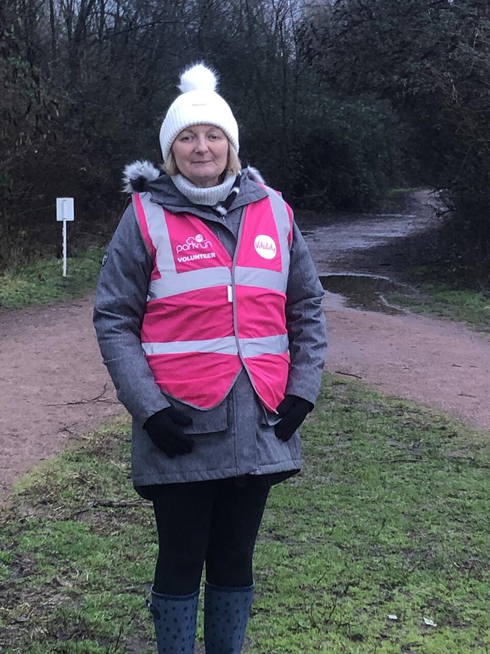 A woman wearing a high viz, hat and coat on a grassy trail