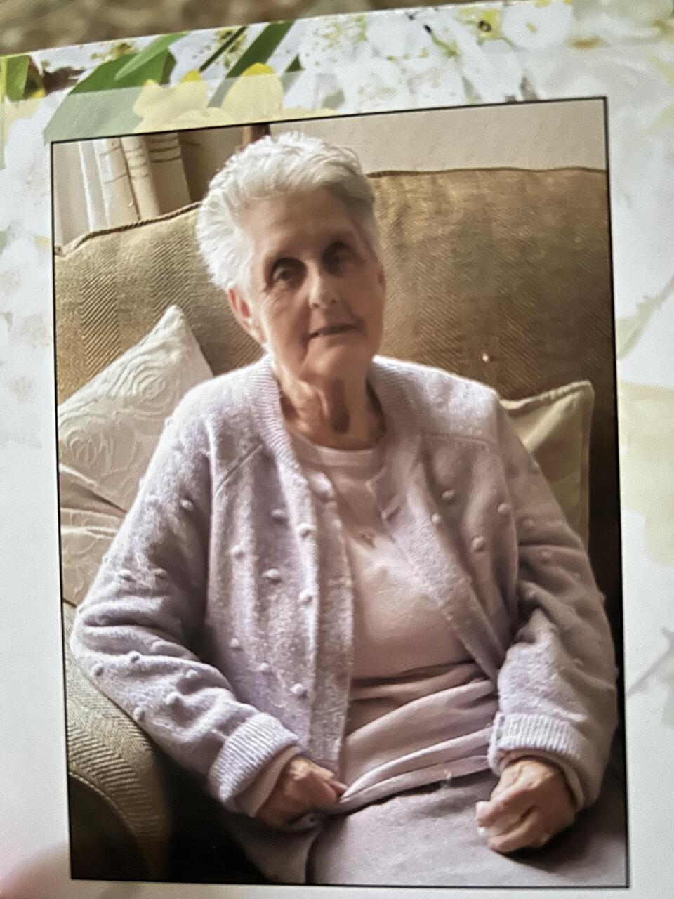 An older woman with short white hair wearing a pink top and cardigan