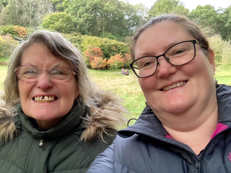 A woman with blonde hair and glasses wearing a green coat and a woman with blonde hair and glasses wearing a blue coat