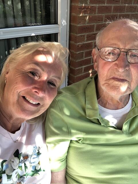 A woman with short blonde hair smiling next to an older bald man wearing glasses and a green t shirt