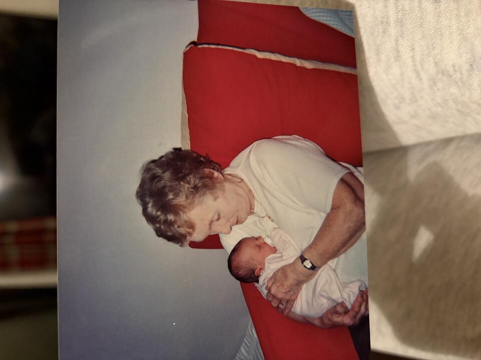 A woman sat on a red chair with short curly blonde hair and a white t shirt cuddling a newborn