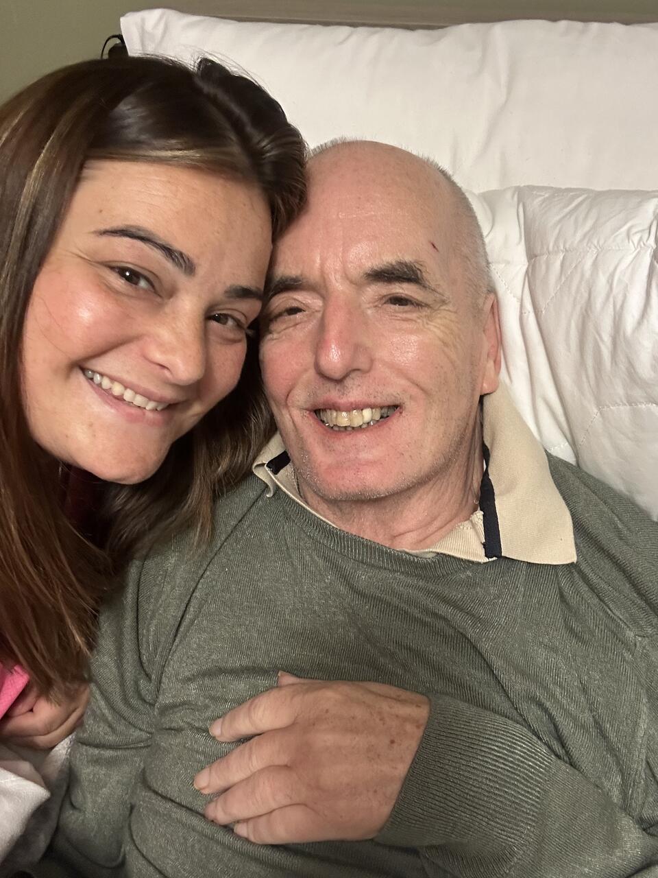 A smiling woman and man, who is resting on two white pillows