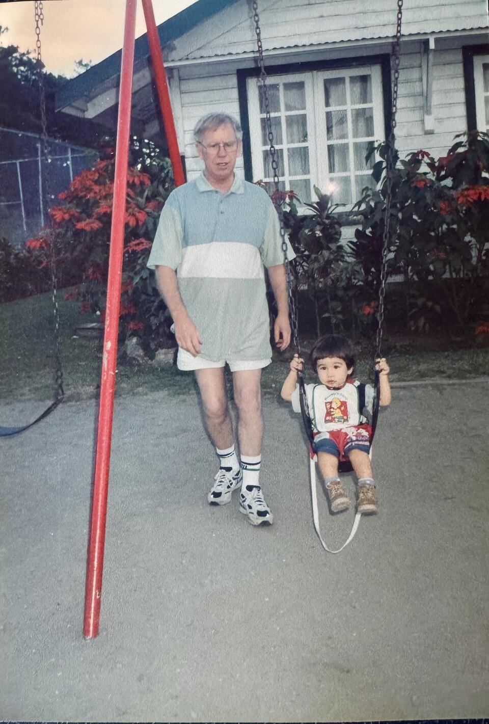 A man stood next to a toddler on a swing