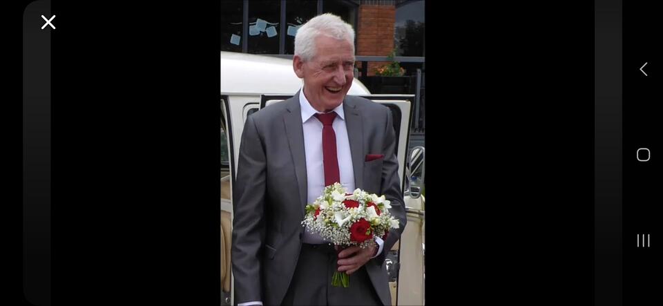 A man in a grey suit with a red tie holding a bouquet of flowers 