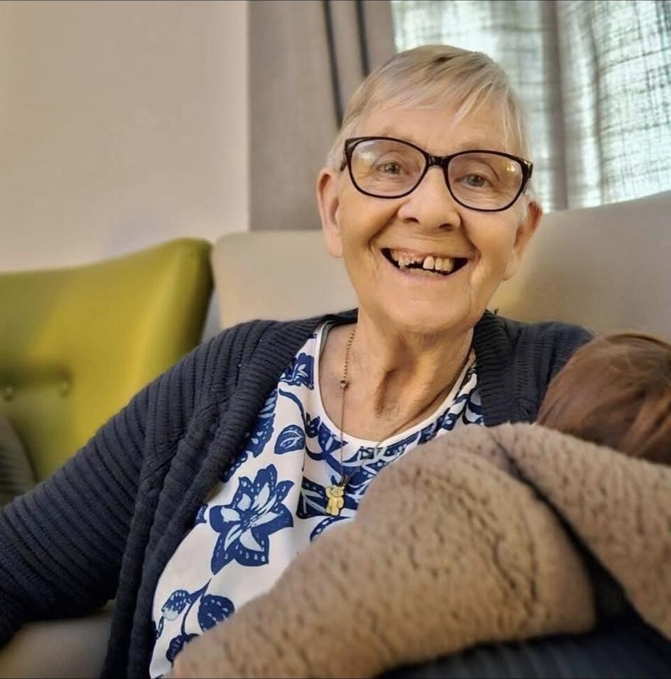 A woman with short blonde hair, glasses, patterned top and blue cardigan holding a brown blanket