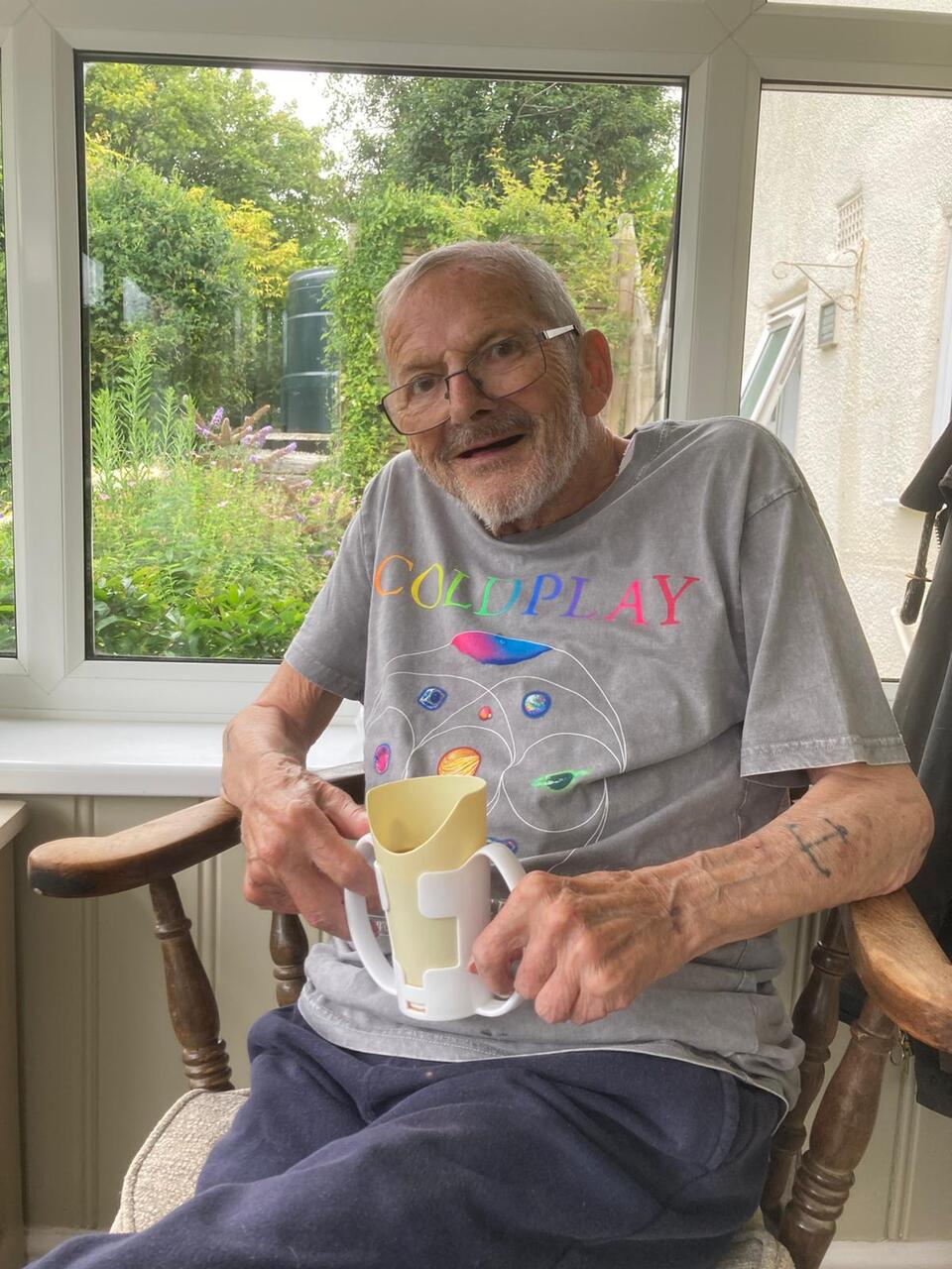 A man holding a cup and smiling sat in a wooden chair