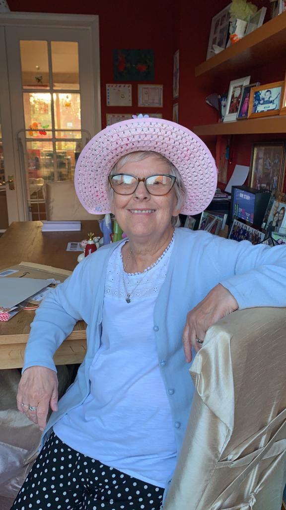 A woman smiling wearing a pink hat, glasses and a light blue top and cardigan