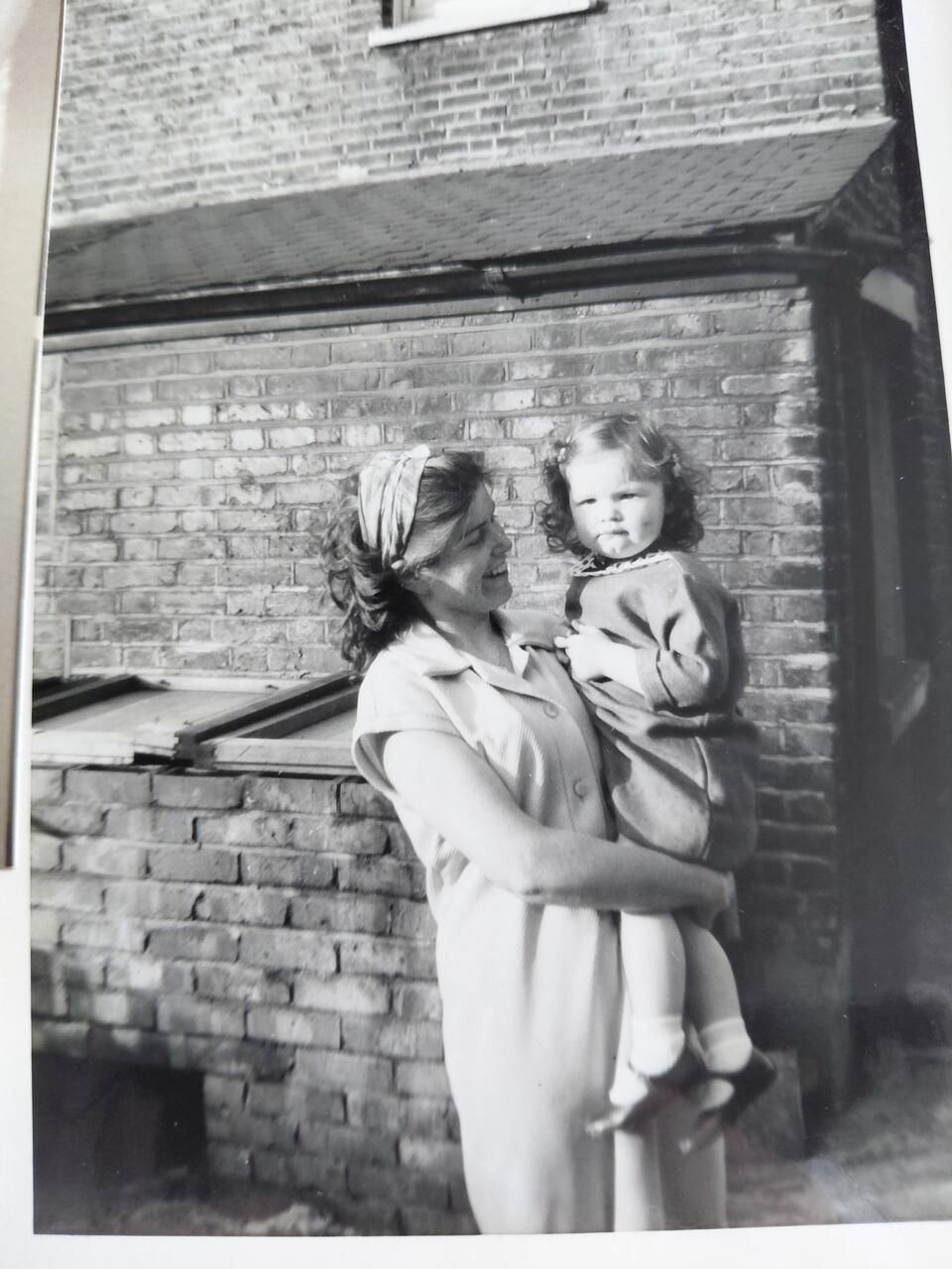 A black and white photo of a woman holding a child in front of a building