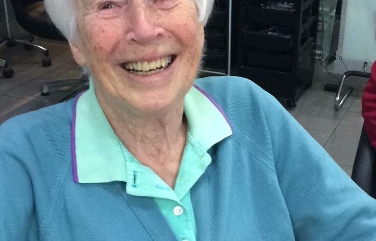 A woman with short white hair wearing a teal shirt and blue cardigan