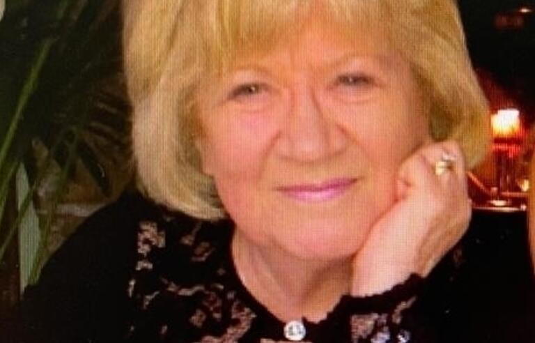 A smiling woman sat at a table with a glass of red wine