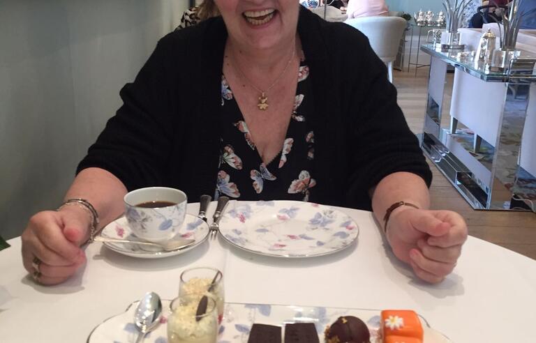 A woman with short grey hair, glasses wearing a dark cardigan at an afternoon tea