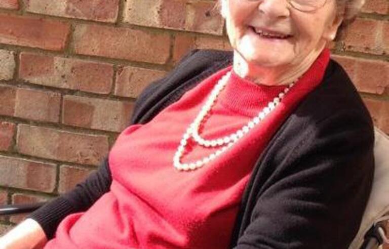 A woman with short light hair wearing a red top, black cardigan and glasses