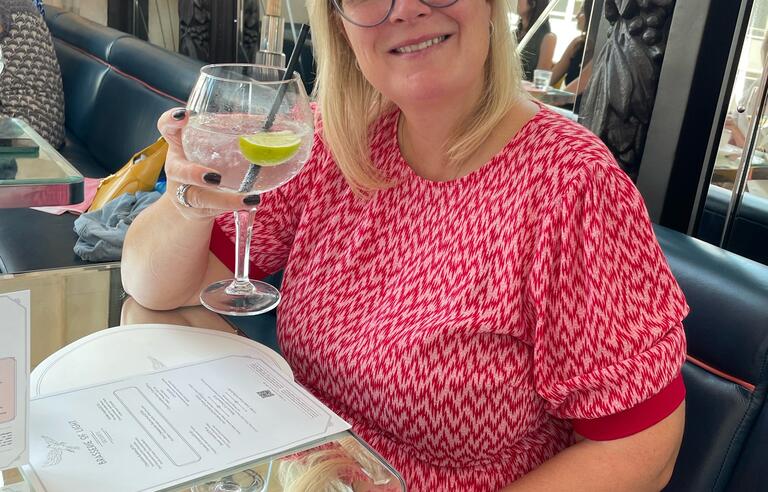 A woman sat at a table, smiling, holding a glass of wine