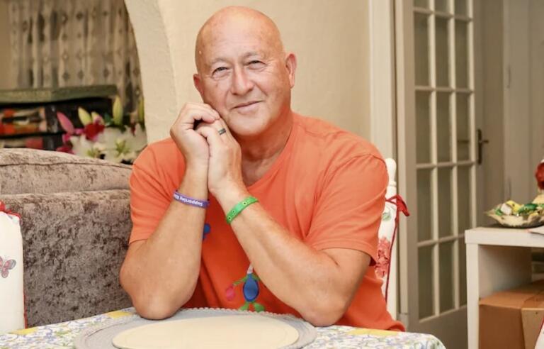 A bald man wearing an orange t shirt sat at a table