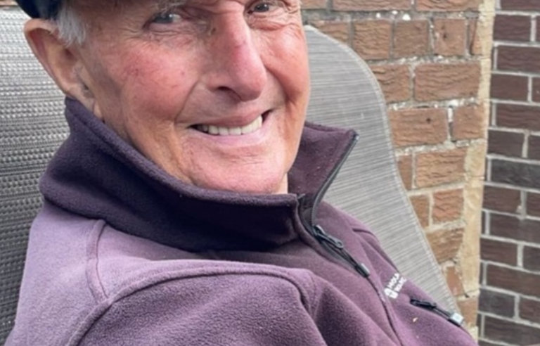 A man sat in a chair wearing a green hat and purple fleece