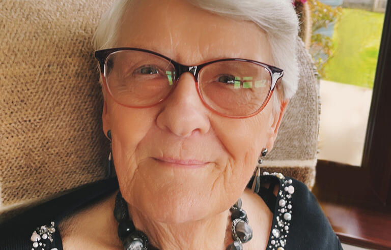 A woman with short grey hair, black glasses, black necklace and black top sat in a chair