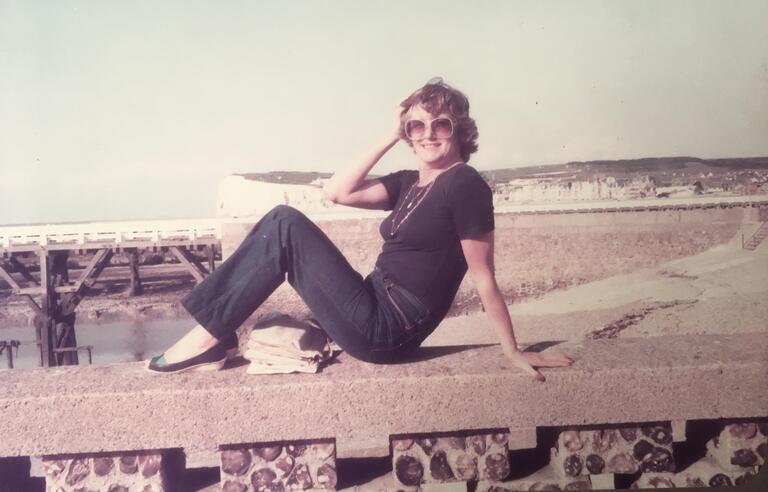 A woman sat on a wall with a beach in the background