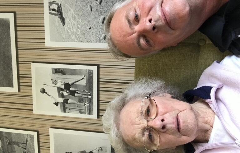 A woman with short grey hair wearing glasses and a pink fleece and a man with grey hair wearing a dark top