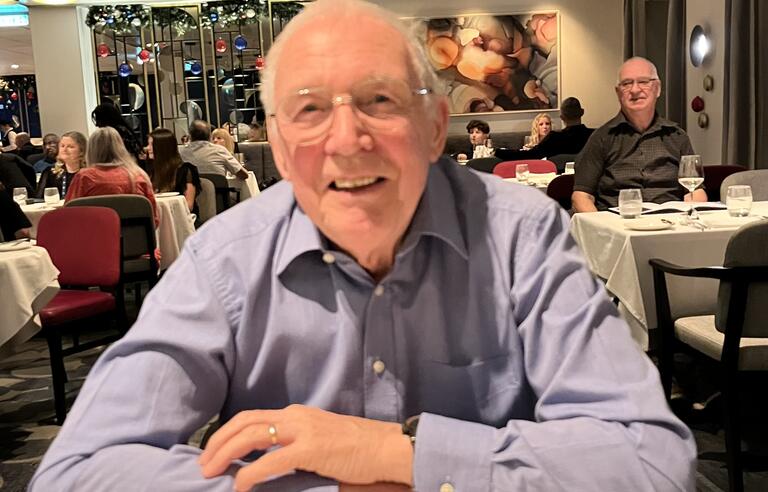 A man smiling, sat at a table in a restaurant 