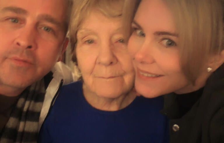 A man with grey hair, an older woman with short blonde hair and a purple top and a woman with blonde hair in an up do wearing a black top