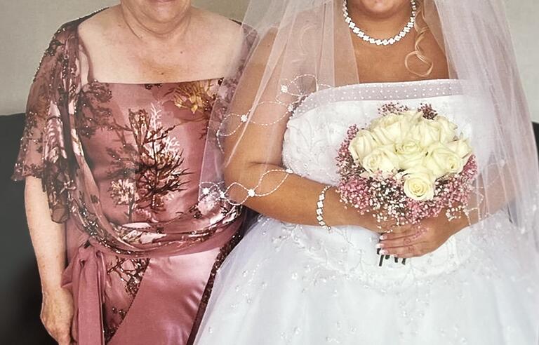 A woman with short blonde hair wearing a pink dress stood next to a bride holding a bouquet