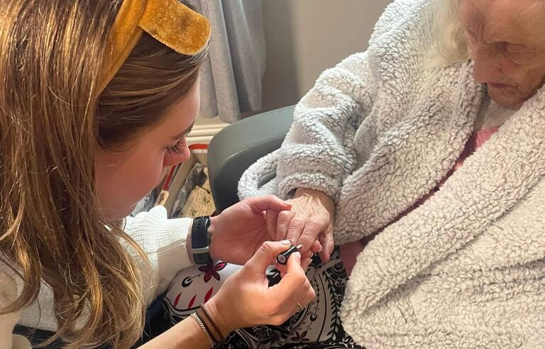 A woman wearing reindeer antlers painting the nails of an older woman sat in a chair
