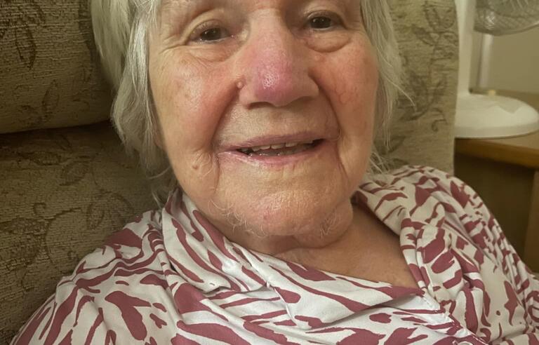 A woman with short white hair wearing a patterned pink and white top