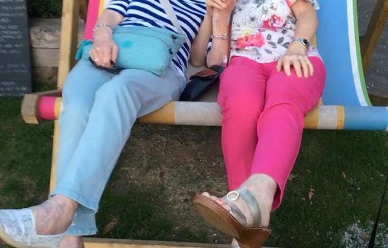 Two women sat on a oversized striped deckchair