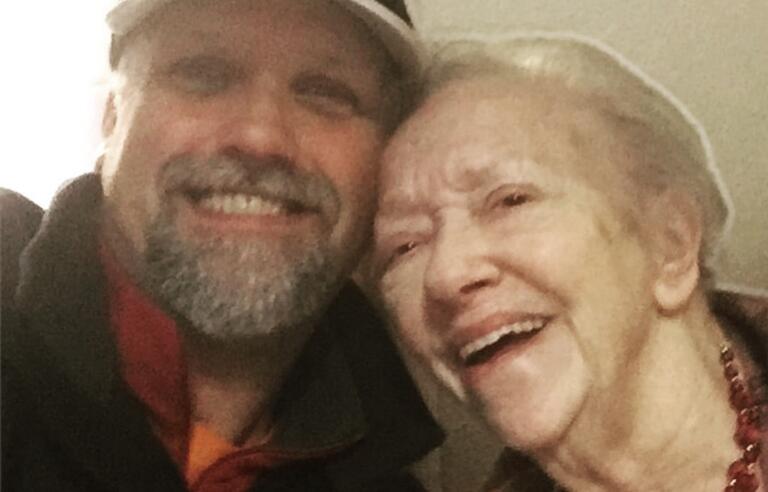 A man wearing a cap and black fleece with a grey beard and a woman with short, light hair wearing a red necklace and dark top